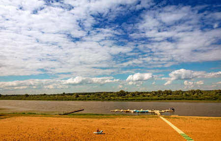 A small river with a pier for catamarans and a sandy beach on the shore on a clear Sunny day.