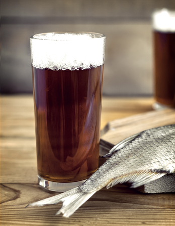 On a wooden table two glasses of beer, next to the cutting Board dried fish and a knife.の写真素材