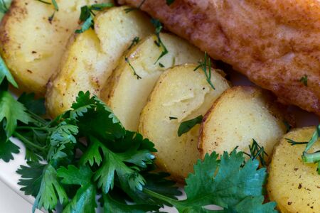 On the table on a plate two slices of fried fish, fried potatoes , dill, parsley. Presented in close-up.の写真素材