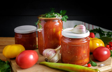 In glass jars Lecho of canned bell peppers and tomatoes, near fresh peppers and tomatoes