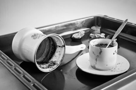 Side view of an empty coffee Cup with coffee stains on the bottom and an empty dirty coffee mug after finishing drinking. Dirty Cup and Turk on a metal tray, black and white image. Copy space.の写真素材