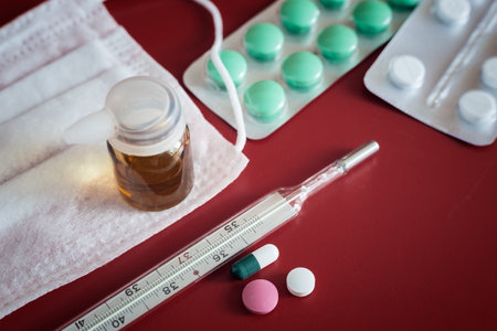 Medicines for the treatment of flu, colds on a red background: face mask, thermometer, pills, nose...