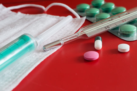Medicines for the treatment of flu, colds on a red background: face mask, thermometer, pills, nose...