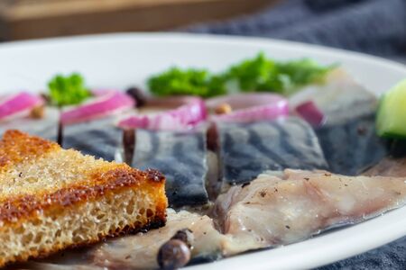 On a wooden table on a napkin plate with pieces of salted mackerel, onions, parsley and a piece of bread. Presented in close-up.の写真素材