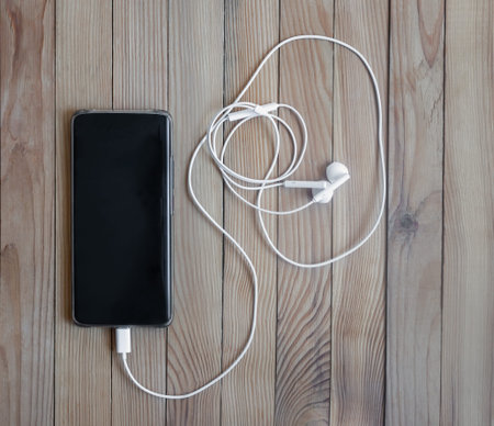 Smartphone and headphones on a wooden background.