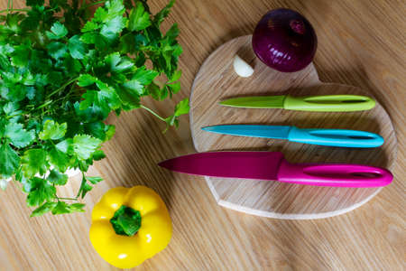 Set of bright knives on a chopping board with vegetables and fresh parsleyの写真素材