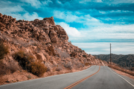 Winding empty road deep in the mountains of the Mojave Desert in California. Bright cloudy sky.