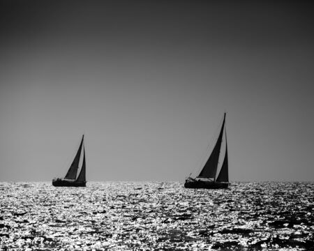 Black and white image of two yachts silhouette in high seaの写真素材