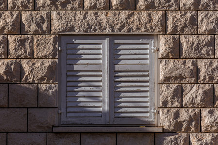 Light brown brick wall with paving stone texture, white framed window with white wooden blinds