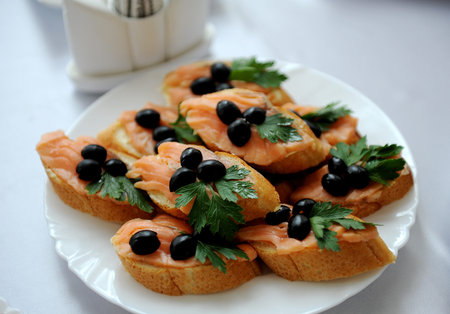 Sandwich with red fish, olives ang parsley on white plate