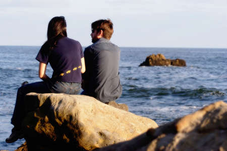 Couple sitting on a rock looking at the oceanの写真素材