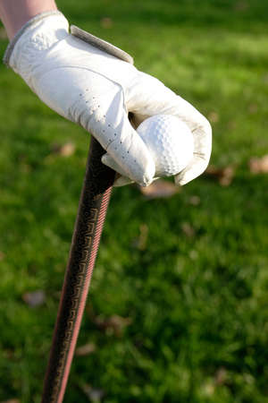 Golfer's hand holding a golf ball and club wearing a white leather gloveの写真素材