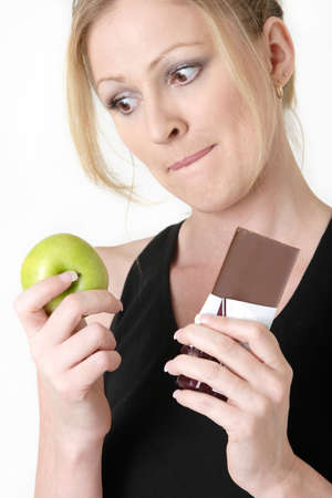 woman holding an apple and chocolate bar trying to decide which one to eatの写真素材