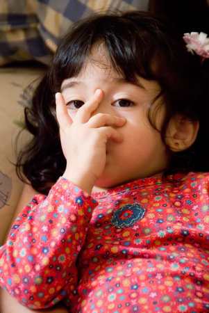 cute little dark haired girl with pig tails up close sucking on thumbの写真素材