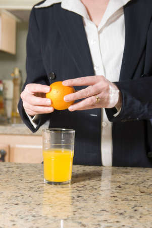 Stock photo of a woman wearing a business suit standing in kitchen with a glass of orange juice and orange in her handの写真素材