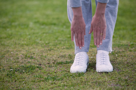 Feet of a woman outside standing on the grass bending down with hands reaching to touch feetの写真素材