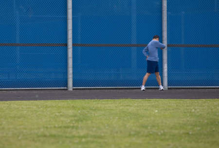 Man outside standing on the grass twisting at the waist for a warm up before starting to run on an outdoor trackの写真素材