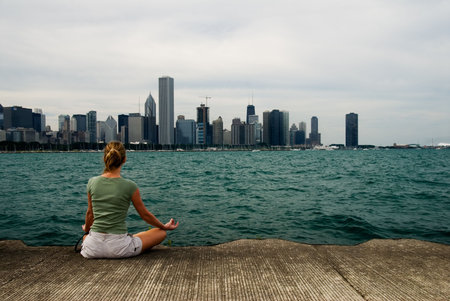 Young woman doing meditation exercise by Lake michigan with city view of downtown chicagoの写真素材
