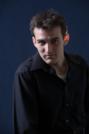 Portrait of handsome brunette young man wearing black dress shirt on dark background