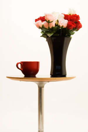 Small end table with a black vase full of red and pink roses beside a big red coffee mugの写真素材