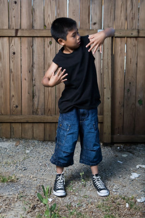 Young asian boy standing outside beside a tall wooden fence wearing jeans and black tshirtの写真素材