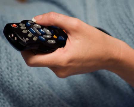 Hand of a woman holding onto a universal remote control channel changer