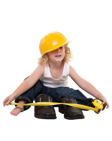 Adorable little blond curly hair three year old boy wearing white muscle top and jeans and yellow hard hat sitting on floor with tape measure measuring grown up mans shoesの写真素材