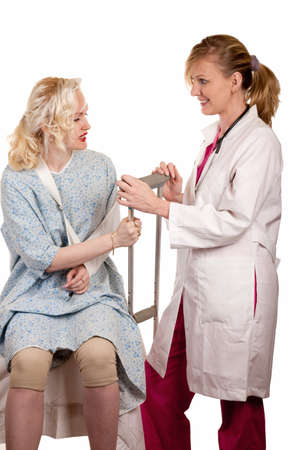 Blond woman doctor standing beside female patient wearing an arm sling and holding a crutchの写真素材