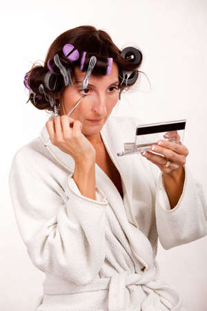 Brunette woman with hair in rollers applying eyeshadowの写真素材