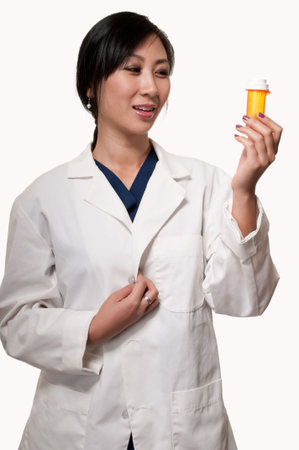 Attractive asian woman in white lab coat holding and looking at a prescription bottle の写真素材