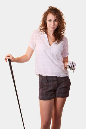 Attractive curly hair woman dressed in sports attire holding a golf club standing on white backgroundの写真素材