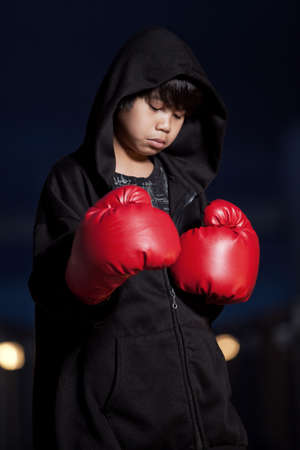 Young intense asian boy wearing boxing gloves preparing for a street fightの写真素材