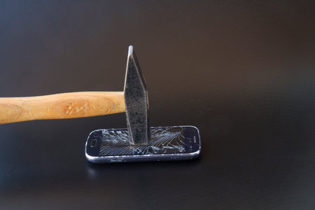 A broken smartphone with a hammer on a dark background