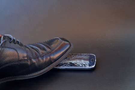 A broken smartphone with a shoe on a dark backgroundの写真素材