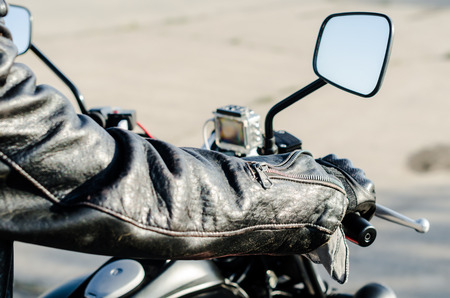 hands of a motorcyclist in a black leather jacket and gloves on the handlebars of a motorcycleの写真素材