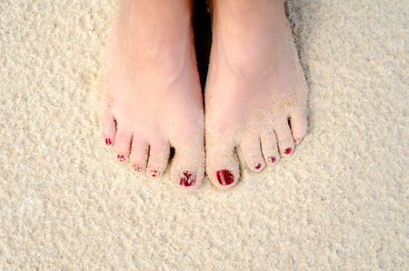 female legs with a red pedicure on the sea sand on the beach closeupの写真素材