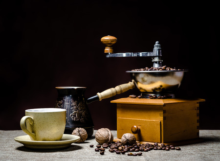 coffee cup with a cezve and coffee grinder with coffee beans and nuts on a dark backgroundの写真素材