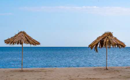 damaged two straw beach umbrellas on an empty seashore on a clear dayの写真素材