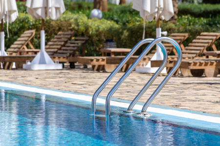 handrails by the pool with blue water on the background of sun loungers and folded white umbrellasの写真素材