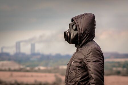 man in a gas mask and a hood amid smoke from factory pipes close upの写真素材