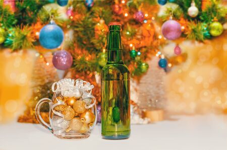 shiny christmas balls in a beer glass next to a green bottle and a decorated new year treeの写真素材