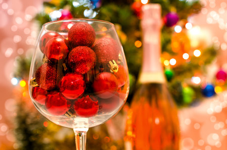 red glitter balls in a large wine glass close up against the background of a decorated Christmas treeの写真素材