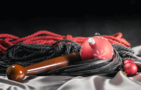 bdsm still life black leather whip and red christmas balls on silver fabric