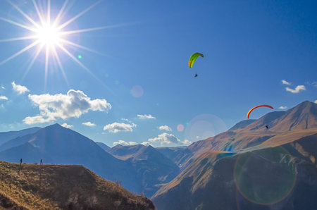 paragliders and tourists  mountains of the Caucasus with sun flare in clouds