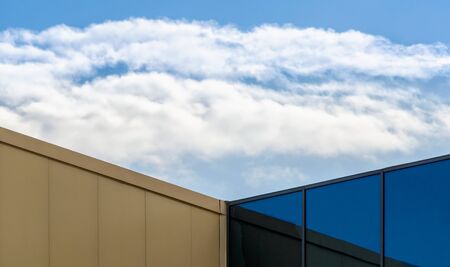 corner of a modern office building with a window and a blue sky with white cloudsの写真素材