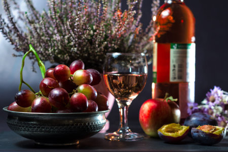 still life of ripe grapes with a glass of wine with an apple with plums and flowers