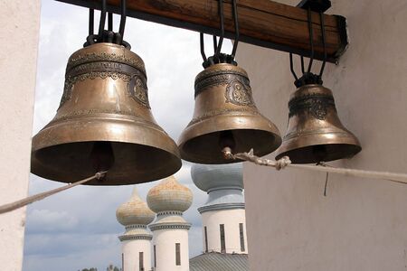 three bells on a bell tower and a churchの写真素材
