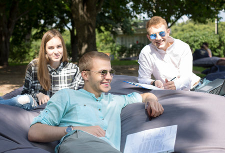 Three happy smiling students relaxing outdoors on a big cushion