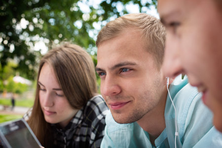 Smiling young thoughtful guy relaxing outdoors  and listening to