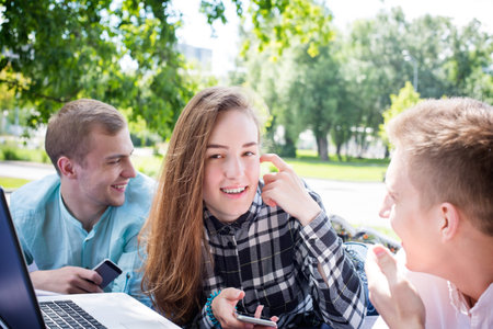 Young happy smiling girl with two male friends relaxing outdoorsの写真素材